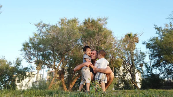 Padre joven abrazando a sus hijos en el parque. Concepto de familia feliz —  Fotos de Stock