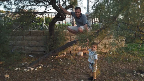 Padre sentadillas en el árbol para enseñar a los niños a jugar al aire libre. — Foto de Stock