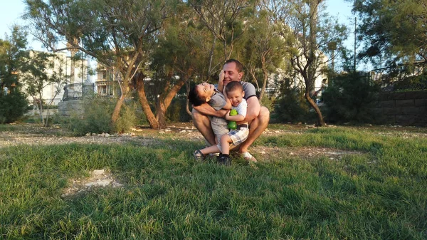 Il giovane padre che abbraccia i suoi figli nel parco. Concetto famiglia felice — Foto Stock