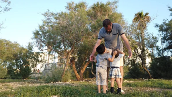 Padre joven abrazando a sus hijos en el parque. Concepto de familia feliz — Foto de Stock