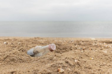 Kum üzerinde boş cam şişe. Çöp sahilde. Deniz kıyısında. Çevre kirliliği. Gezegeni kurtarmak. Ekolojik sorun. Kirli kıyı şeridi. Doğa teması.