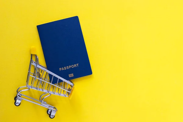 Biometric passports in mini shopping cart on yellow baclground. Business trip and travel, online shopping concept. Top view, flat lay with copy space.