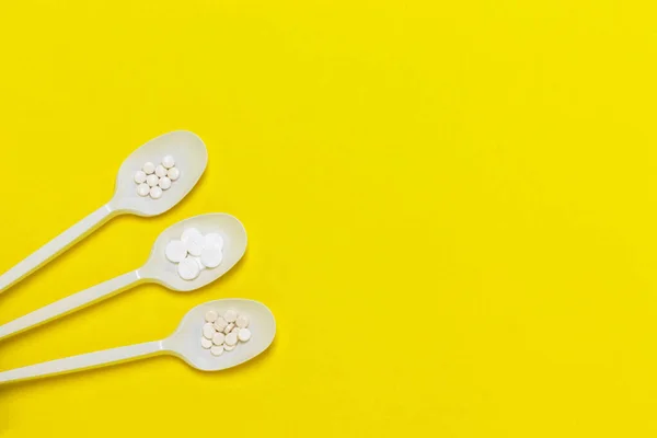 Sarı arka planda hapları olan üç plastik kaşık. İlaç sanayisi. Salgın, ağrı kesici, sağlık ve tedavi konsepti. Düz yatıyordu. Kopyalama alanı olan üst görünüm.