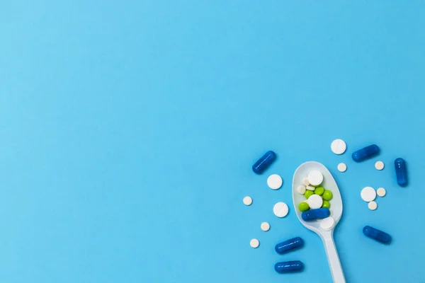 Mavi arka planda plastik kaşıkta haplar ve kapsüller. İlaç sanayisi. Salgın, ağrı kesici, sağlık ve tedavi konsepti. Düz yatıyordu. Kopyalama alanı olan üst görünüm.