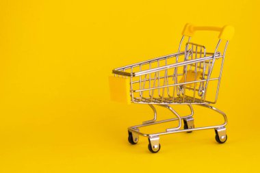 Sarı arka planda izole edilmiş mini alışveriş arabası. Boş süpermarket arabası. Çevrimiçi konsept. Boşluğu kopyala