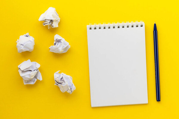 Blank notepad, pen and crumpled paper balls on bright yellow background. Writing message. ?rawing up a plan. New or bad idea concept. Draw up plan. Flat lay, top view, copy space.