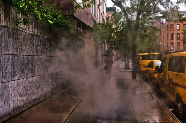 New York City, ABD, Mayıs 2019, yağmurlu bir günde havalandırma deliğinden geçen şemsiyeli bir yaya ve park halindeki bazı taksiler