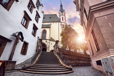 Czech Krumlov, Czech Republic. Streetview at Saint Vitus Catholic church entrance from the medieval antique street with old houses during sunset. Popular travel destination in Europe.