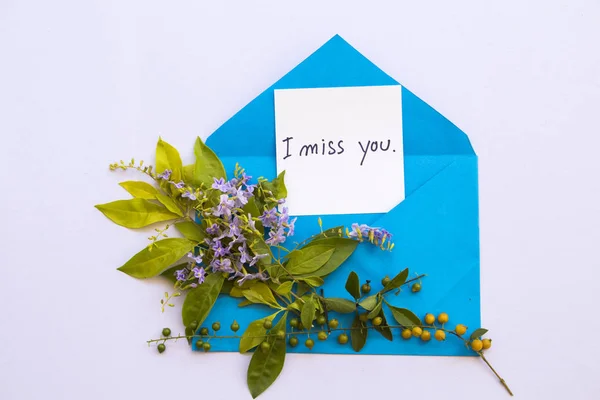 i miss you message card handwriting in blue envelope with purple flowers arrangement on background white