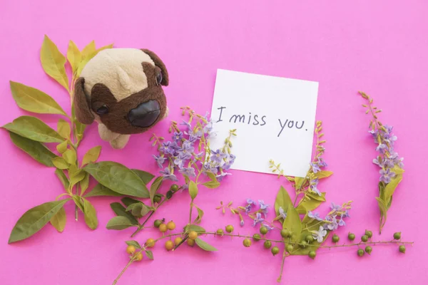 i miss you message card handwriting and dog toy with purple flowers arrangement on background pink