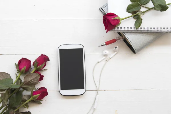 mobile phone and notebook planner with rose flower on background white wood