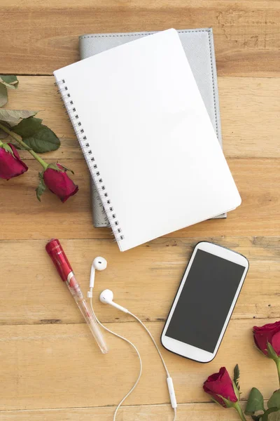 mobile phone and notebook planner with rose flower arrangement on background  wood