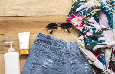 Cilt yüz güneş kremi spf50, güneş gözlüğü, kısa kot pantolon ve gömlek bir kadın için doğal kozmetik relax ahşap zemin üzerine yaz