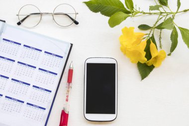 defter Takvim Planlayıcısı ve cep telefonu arka plan beyaz tahta üzerinde sarı çiçek ile ofis büro iş çalışmak için