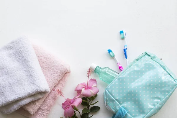 terry cloth ,mouthwash ,toothbrush health care for oral cavity in blue bag travel with pink flowers hibiscus on background white wooden