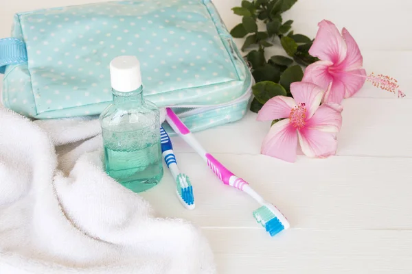 terry cloth ,mouthwash ,toothbrush health care for oral cavity in blue bag travel with pink flowers hibiscus on background white wooden
