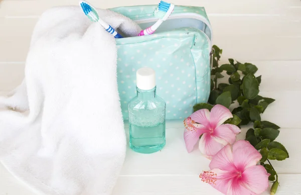 terry cloth ,mouthwash ,toothbrush health care for oral cavity in blue bag travel with pink flowers hibiscus on background white wooden