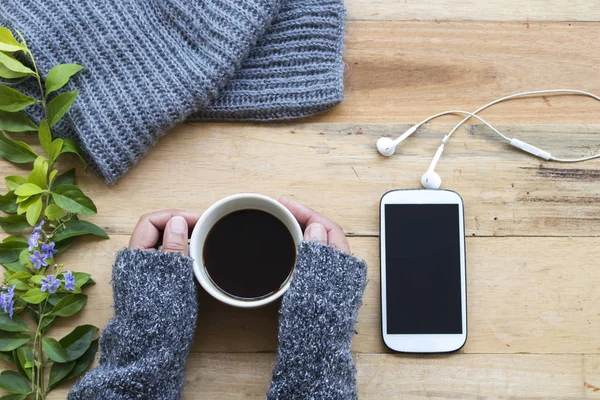 El örgü yün atkı ve yaşam tarzı kadın için cep telefonu ile sıcak kahve tutan kadının relax ahşap arka plan üzerinde kış sezonu