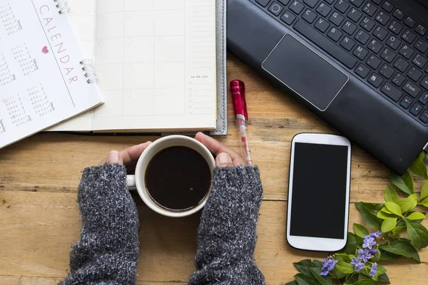 mobile phone ,calendar ,computer for business work and hand of woman holding hot coffee relax in winter season on background  wood at office desk