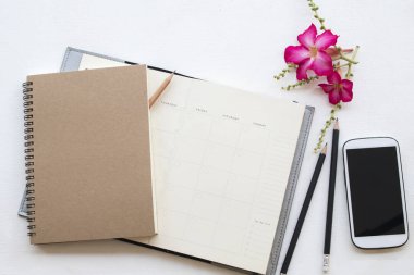 defter planlayıcısı ve cep telefonu iş için iş ile pembe çiçek dekorasyon düz beyaz arka plan üzerinde yatıyordu stili