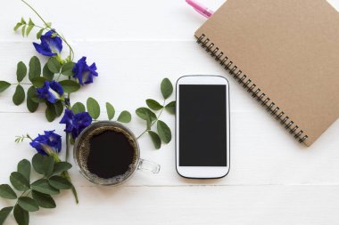 dizüstü bilgisayar, cep telefonu ve sıcak siyah kahve Asya düzenleme düz mavi çiçek kelebek bezelye yerel florası ile stil beyaz arka plan üzerinde yatıyordu
