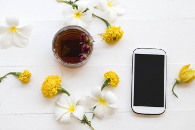 cep telefonu ve bitkisel sağlıklı içecekler sıcak gül çay kokteyl su çiçekler frangipani, kadife çiçeği, kurutulmuş gül aranjman arka plan beyaz tahta üzerinde stil yat