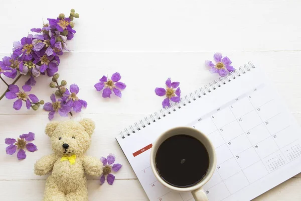 calendar plane with teddy bear ,hot coffee  and purple flowers in spring season arrangement flat lay style on background white wooden