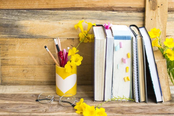 notebook ,dictionary english and all book for study of student  with stationary ,yellow flowers decoration on background wooden