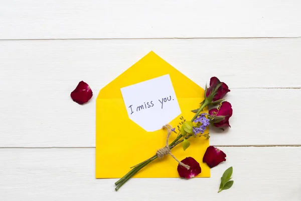 i miss you message card handwriting in yellow envelope arrangement flat lay postcard style on background white wooden