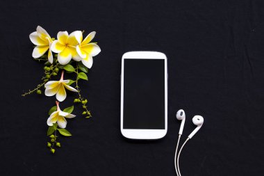 cep telefonu, kulaklık ve sarı çiçekler frangipani düzenleme düz arka plan siyah stil yatıyordu