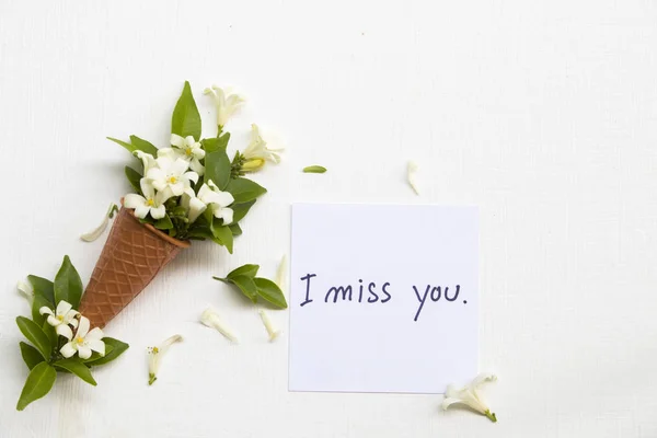 i miss you message card handwriting with white flowers jasmine in cone arrangement flat lay postcard style on background white