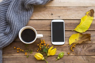 sıcak kahve, örgü yün eşarp, ylang ylang çiçekler, cep telefonu ve yaşam tarzı kadının sarı yaprakları sonbahar sezonu düzenleme düz arka plan ahşap tarzı dinlenmek 