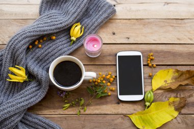 cep telefonu, sıcak kahve espresso , örgü yün eşarp ve sarı çiçek ylang ylang , yaşam tarzı kadın sarı yaprakları sonbahar ve kış aranjmandüz döşeme tarzı arka plan ahşap dinlenmek