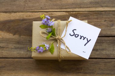 Üzgünüm.Mesaj kartı el yazısı ve hediye kutusu, çiçek aranjmanı düz bir şekilde arkaplan tahtasına yerleştirilmiş.