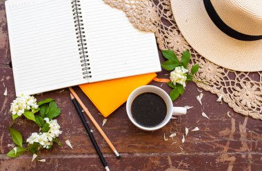 İş için not defteri planlayıcısı sıcak kahve, beyaz çiçekler yasemin, şapka ve örgü ören hayat tarzı kadın yaz aranjmanında rahatla düz bir şekilde arka plan tahtasına uzan