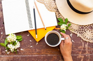 İş için not defteri planlayıcısı sıcak kahve, beyaz çiçekler yasemin, örgü ören iplik ve hayat tarzı kadının eli yaz aranjmanında düz bir şekilde arka plan tahtasına uzanıyordu.