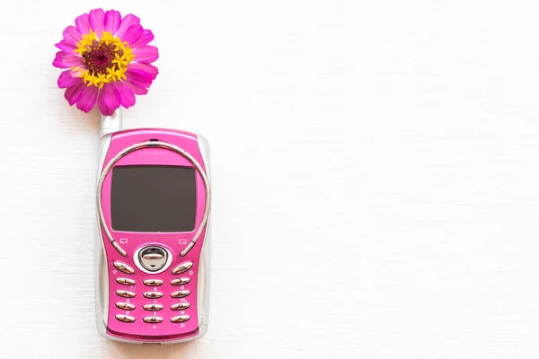 pink older little mobile phone press the button old generation with pink flower zinnia arrangement flat lay style on background white