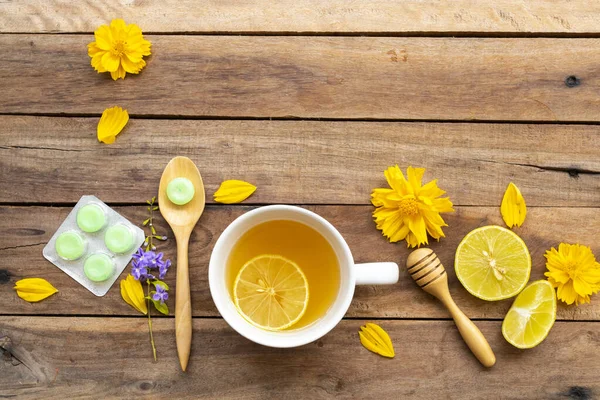 Sağlıklı bitkisel içecekler sıcak bal limonu ve sağlık için pastil limon dilimi ile boğazı ağrıyan limon dilimi, çiçek kainatı arka planda düz bir şekilde yerleştirilmiş ahşap