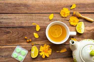 Sağlıklı bitkisel içecekler sıcak bal limonu ve sağlık için pastil limon dilimi ile boğazı ağrıyan limon dilimi, çiçek kainatı arka planda düz bir şekilde yerleştirilmiş ahşap