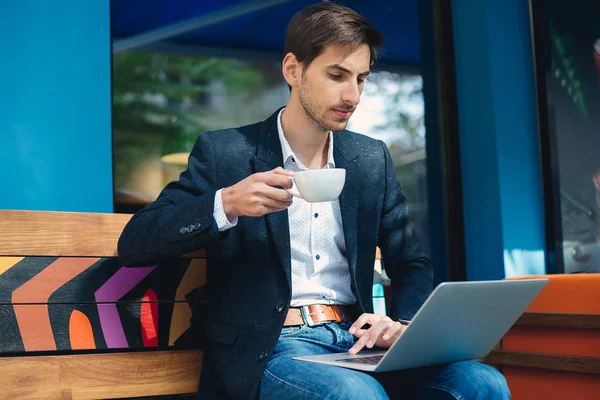 Joven hombre guapo disfrutar del café trabajando en el ordenador portátil — Foto de Stock