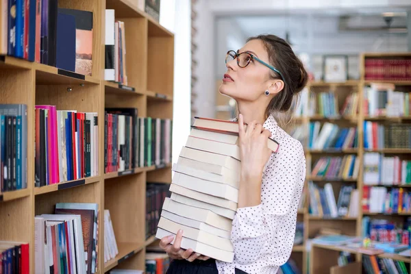 Ung kvinna med en trave böcker i biblioteket — Stockfoto