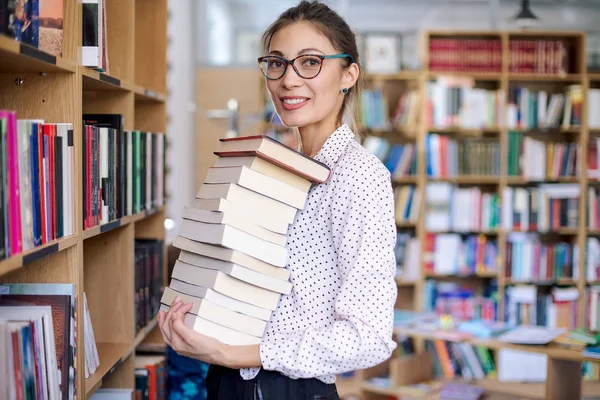 Portrait of young woman with a stack of books in library — Stock Photo, Image