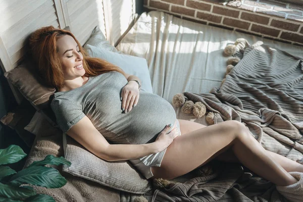 Futura mamma sdraiata sul letto a riposo mentre si tocca la pancia — Foto Stock