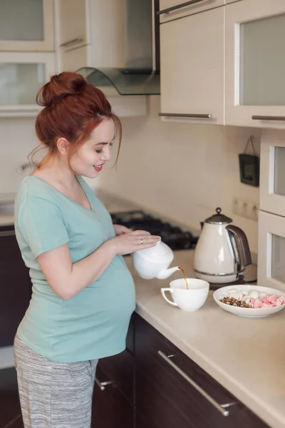 Usmívající se těhotná žena nalévání čaje — Stock fotografie