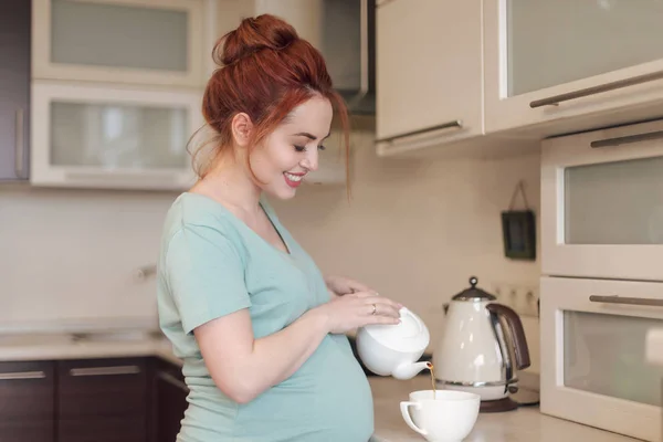 Sorridente donna incinta versando il tè — Foto Stock