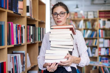 Kitaplıktaki kitapların bir yığınına olan kadın