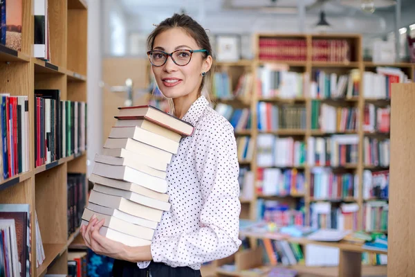 Junge Frau mit einem Stapel Bücher in der Bibliothek — Stockfoto