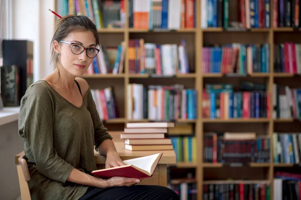 Fiatal, vonzó nő, aki olyan könyv a könyvtárban — Stock Fotó