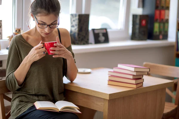 Mulher com óculos lendo um livro com uma xícara de café — Fotografia de Stock
