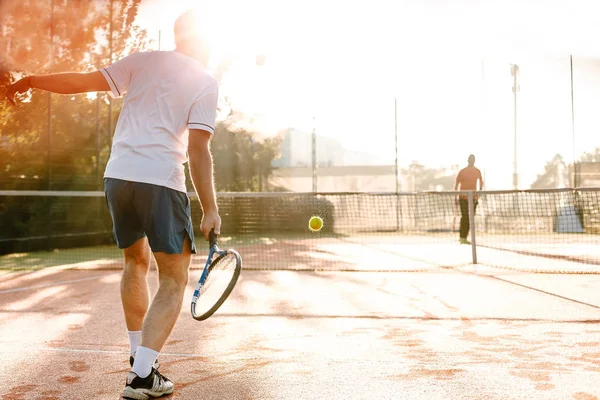 Man playing tennis in the morning in sunlight
